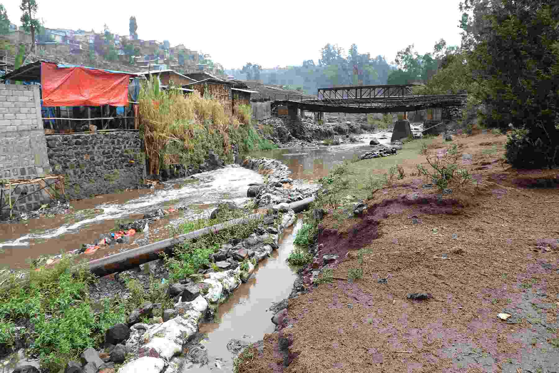 View from the riverbank of a heavily polluted river with discoloured brown water and a large amount of physical waste